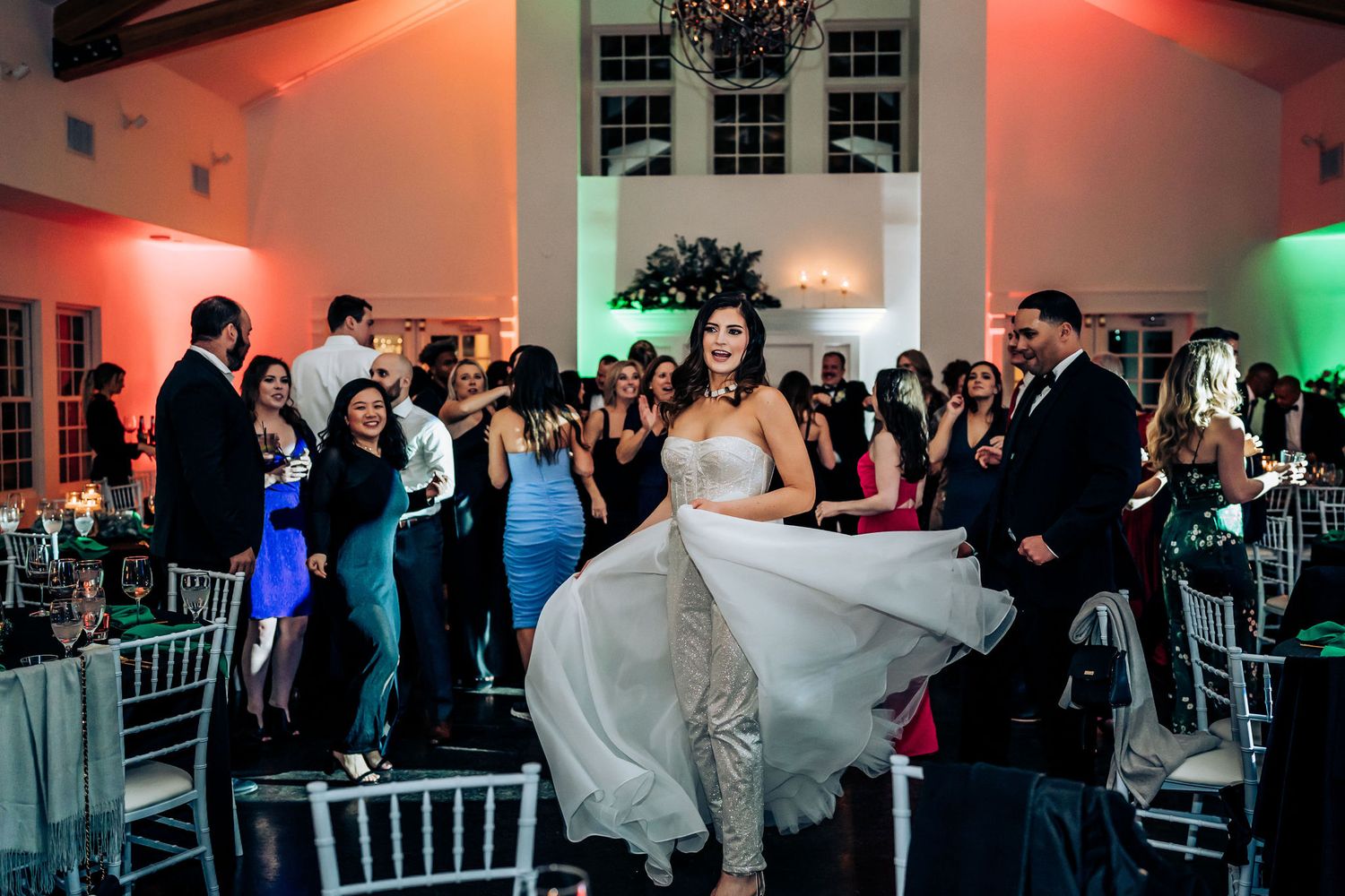 Guests celebrate at a wedding reception with dramatic lighting and silver chiavari chairs.