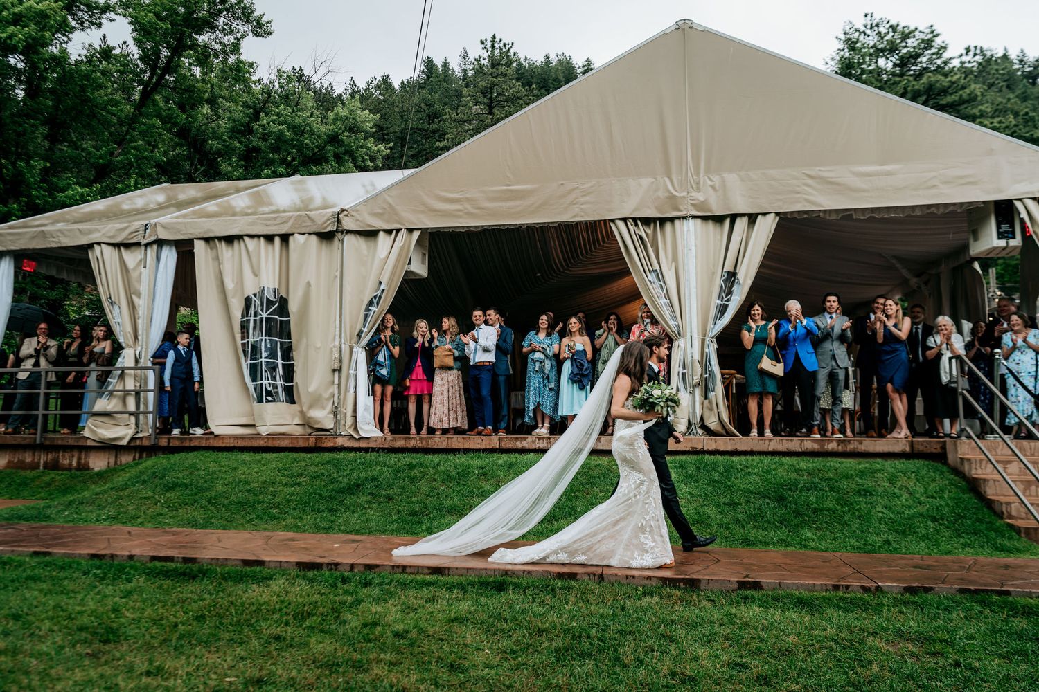 Large beige wedding reception tent set up on grass with guests gathering outside.