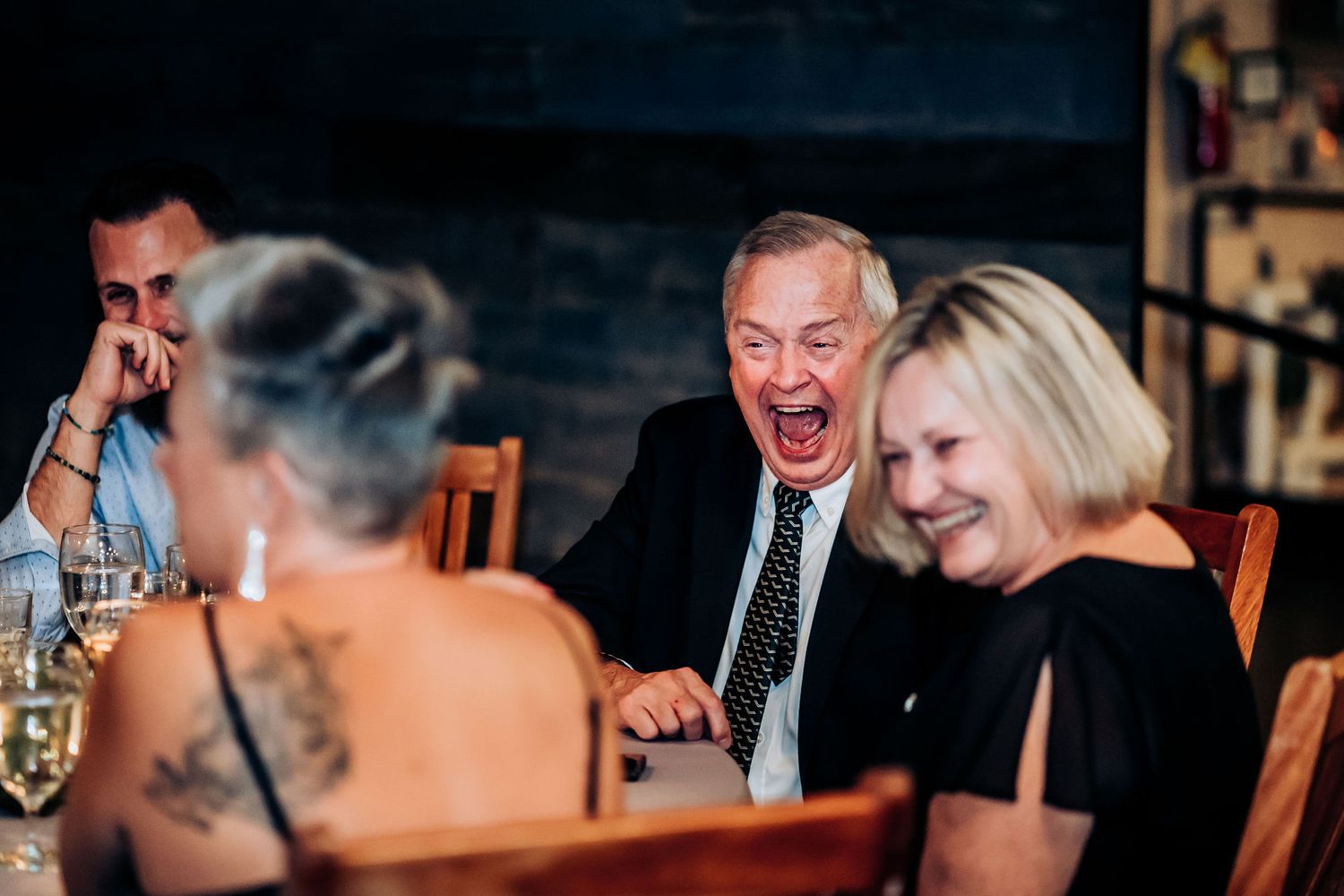 Candid moment of guests sharing laughter during wedding reception dinner.