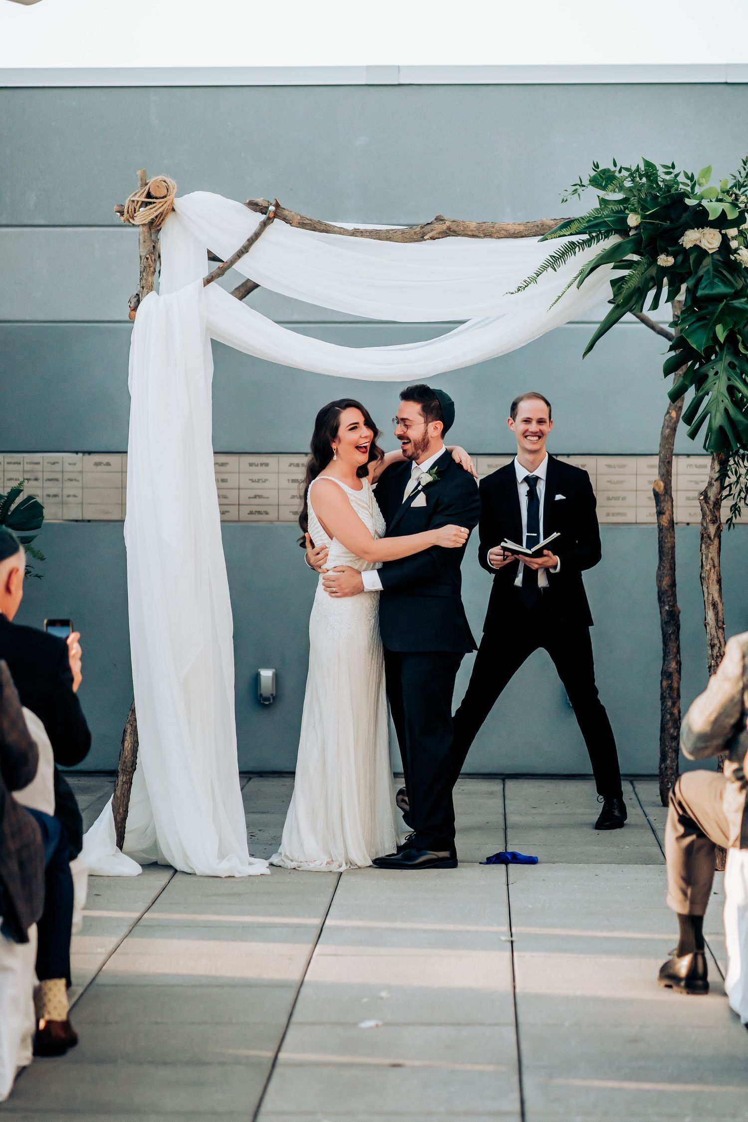 Joyful celebration moment during wedding ceremony under white draped arch with floral details.