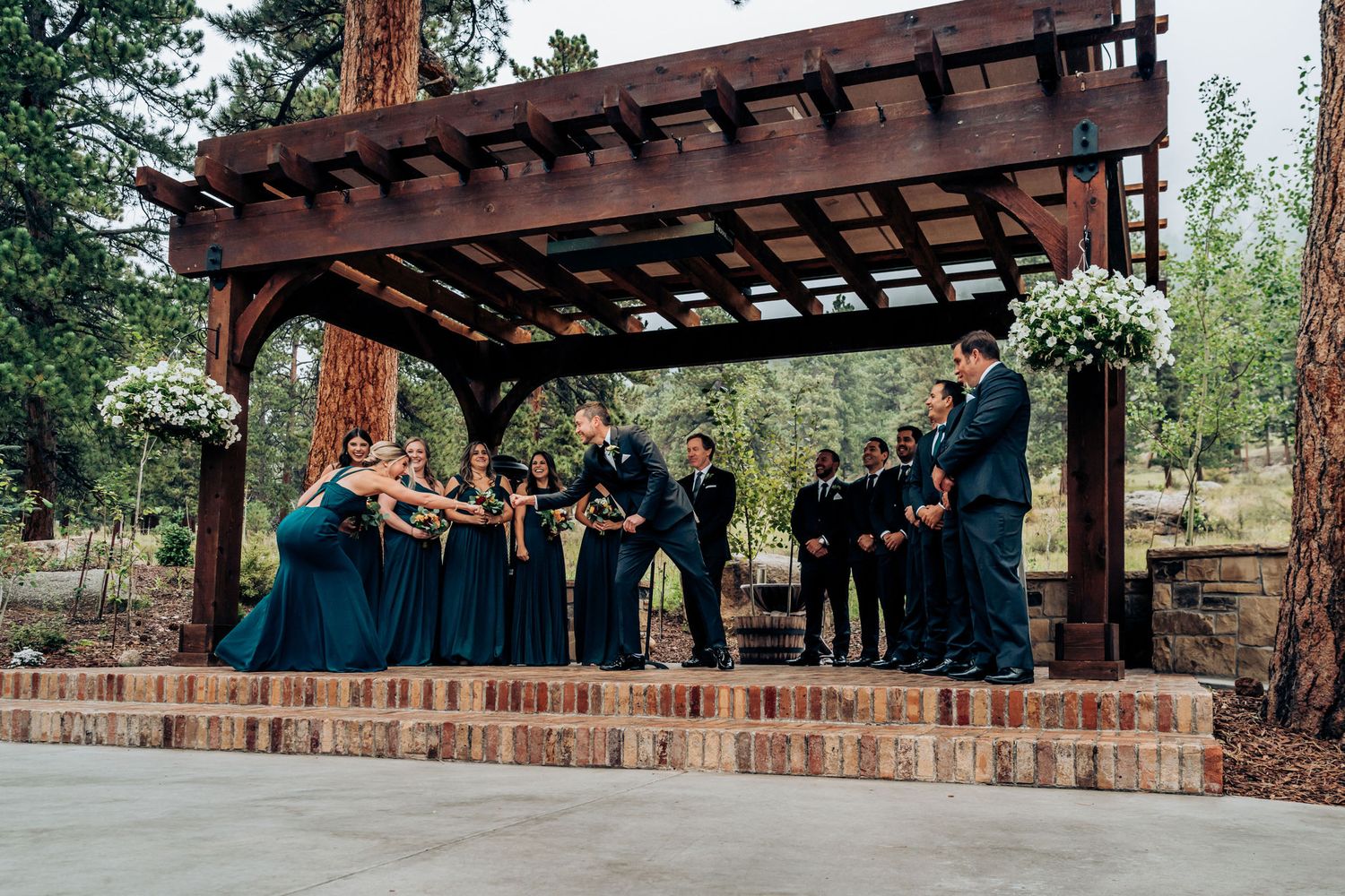 Wedding party stands under a wooden pergola during an outdoor mountain ceremony.