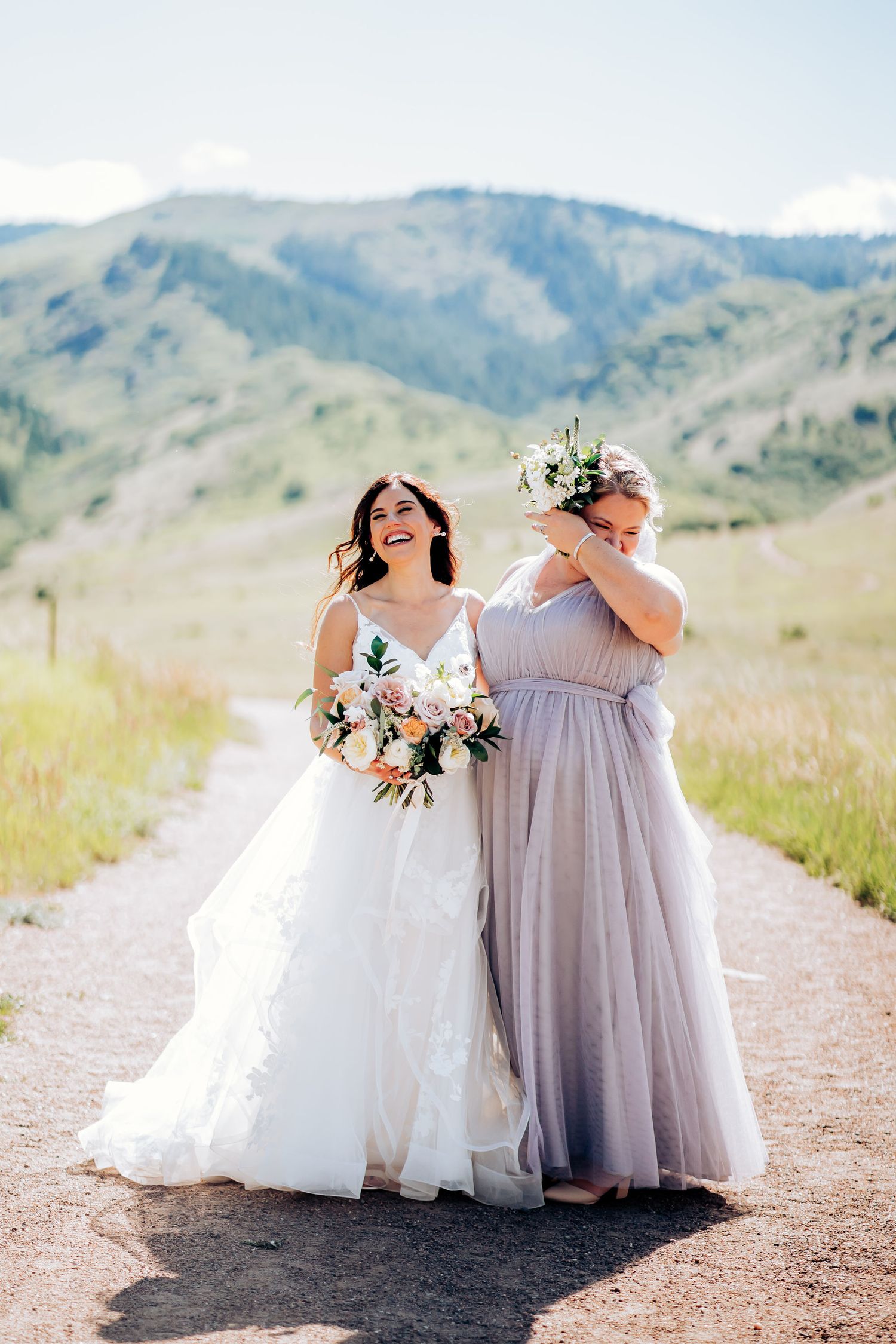 Two people sharing joyful moment in wedding attire on mountain trail.