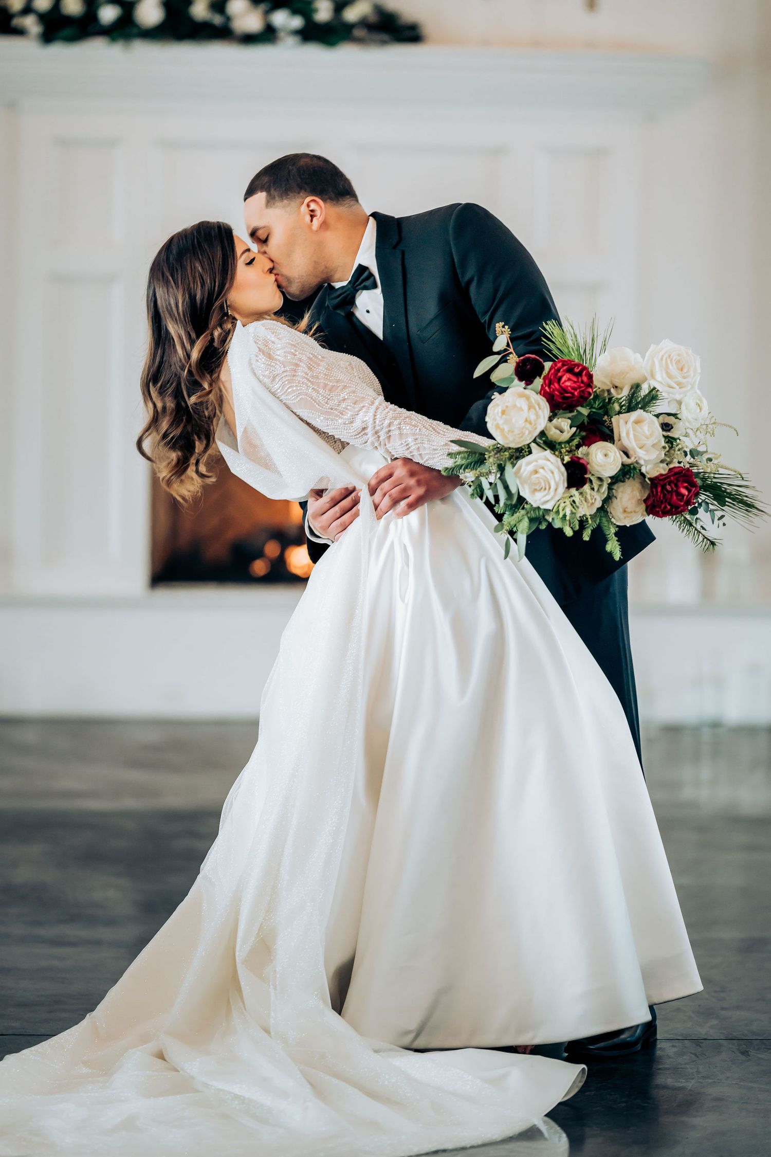 Romantic wedding dance dip pose with bride in long sleeve gown holding floral bouquet.