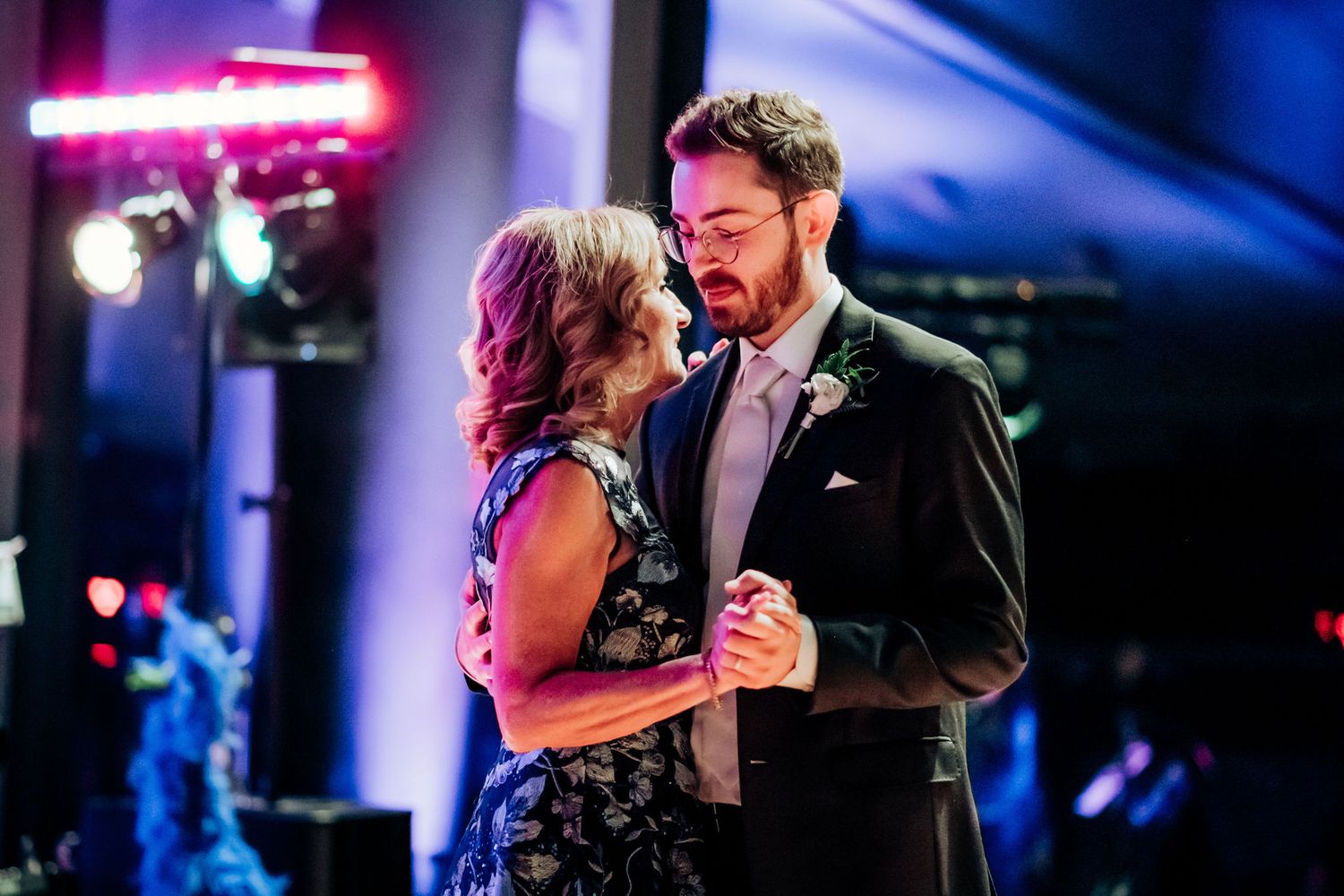 A couple shares a romantic dance under colorful lighting at their wedding reception.