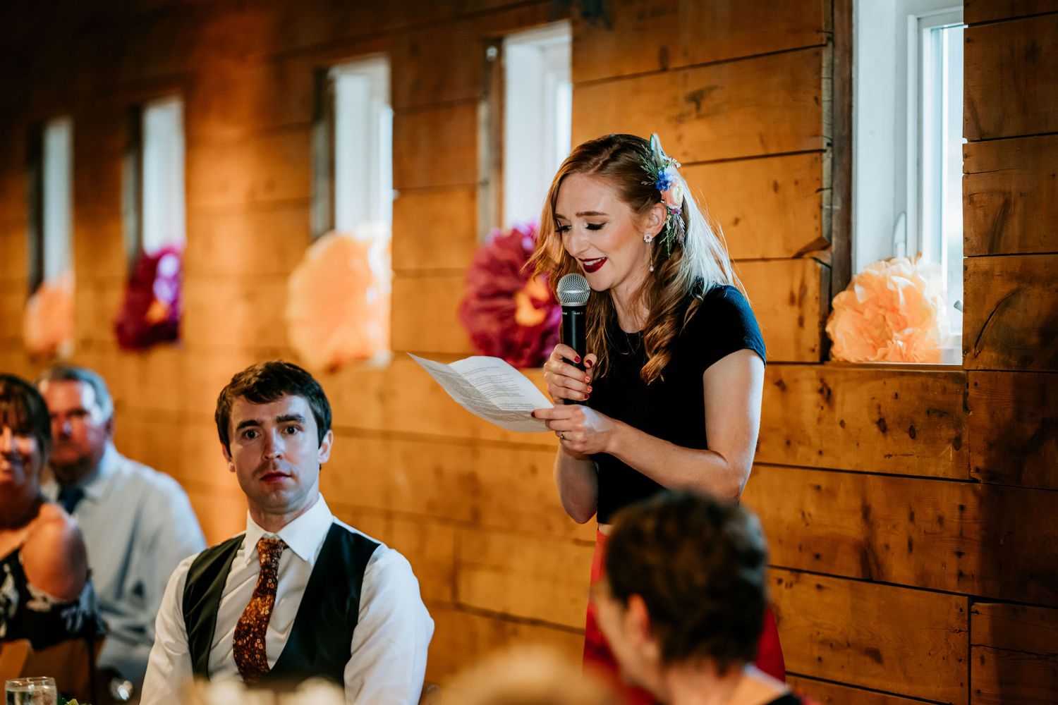 Speech being given at a rustic wooden barn wedding reception venue with string lights and festive decor.