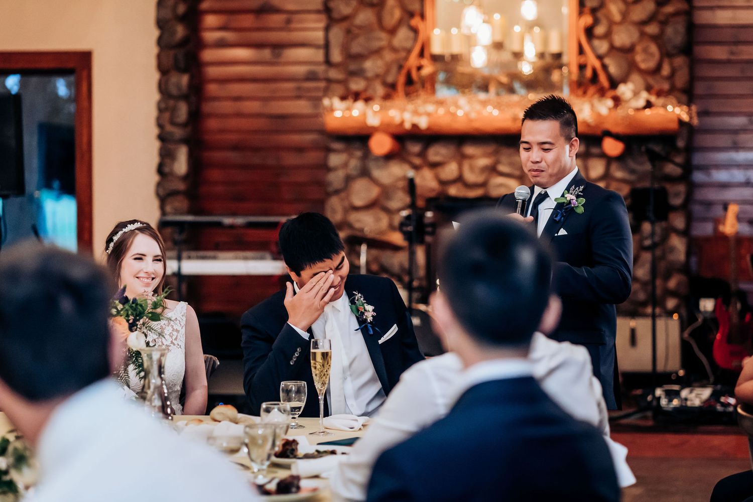 Wedding reception speech in rustic lodge venue with stone fireplace and warm lighting.