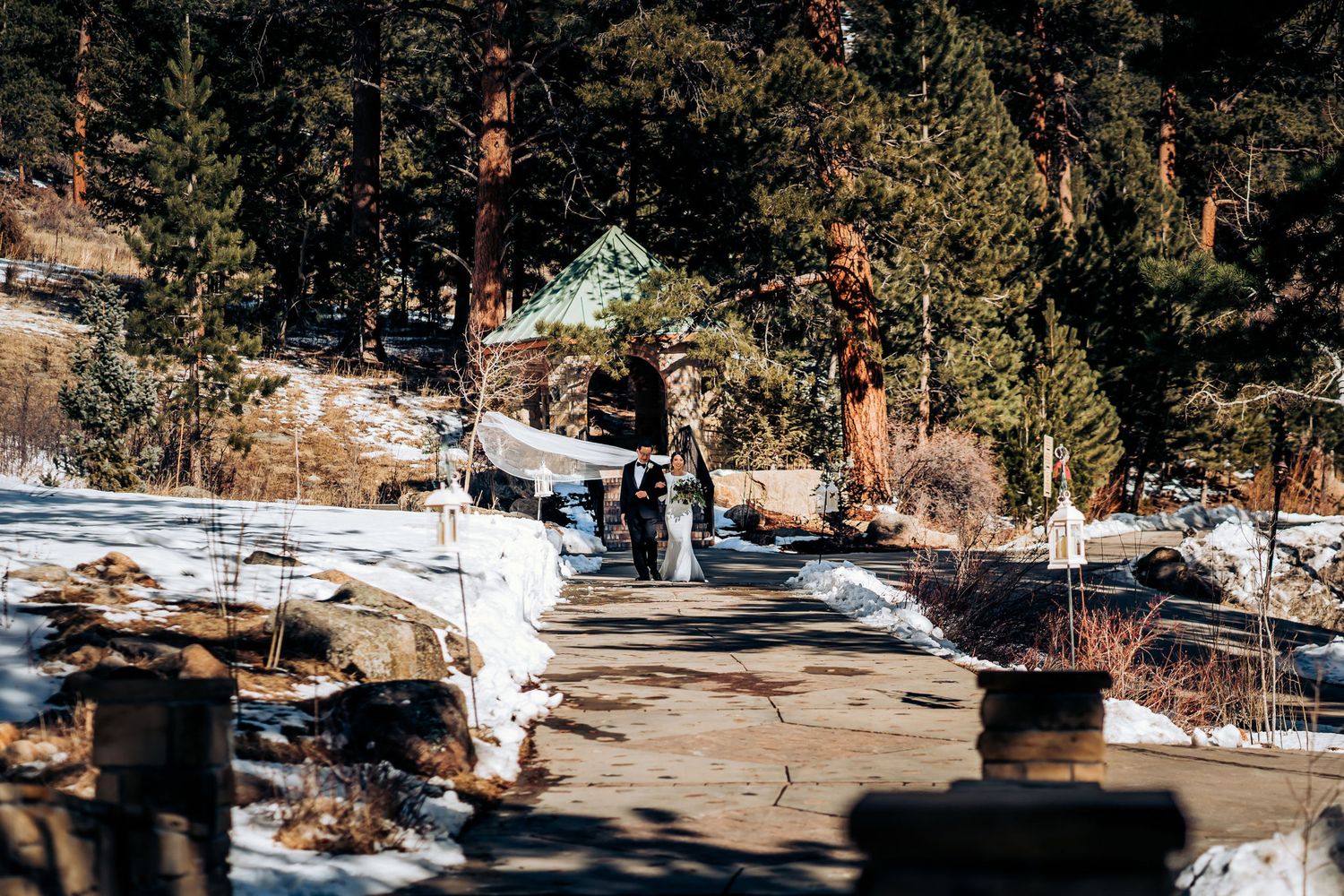 Snow-covered mountain path leading to a rustic wedding venue surrounded by tall pine trees.