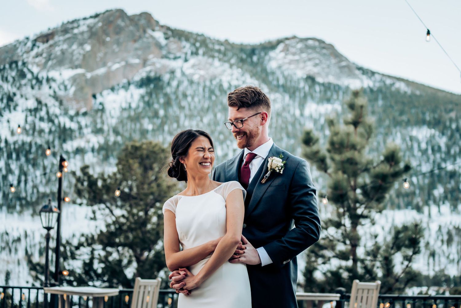 A romantic winter wedding photo with a snow-capped mountain backdrop on an outdoor deck.