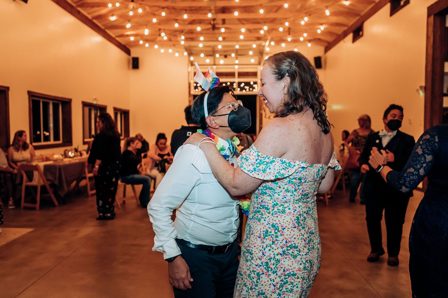 Couple dancing under warm string lights in an indoor venue during celebration.