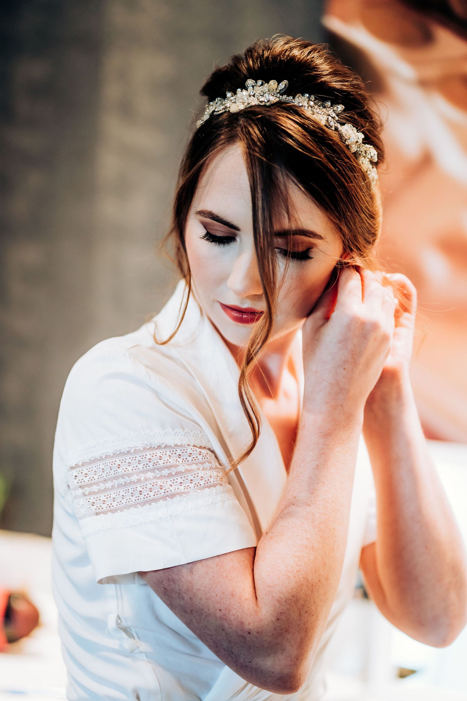 Bride wearing delicate crystal headpiece and white dress during wedding preparations.