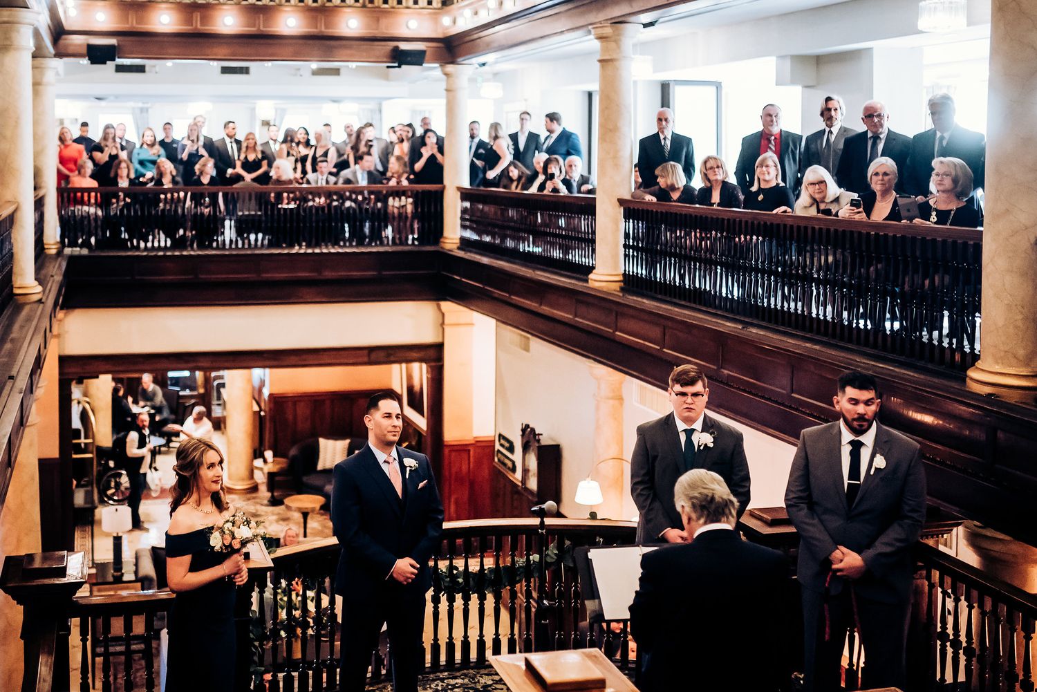 A wedding ceremony taking place on an elegant staircase with guests watching from multiple levels.