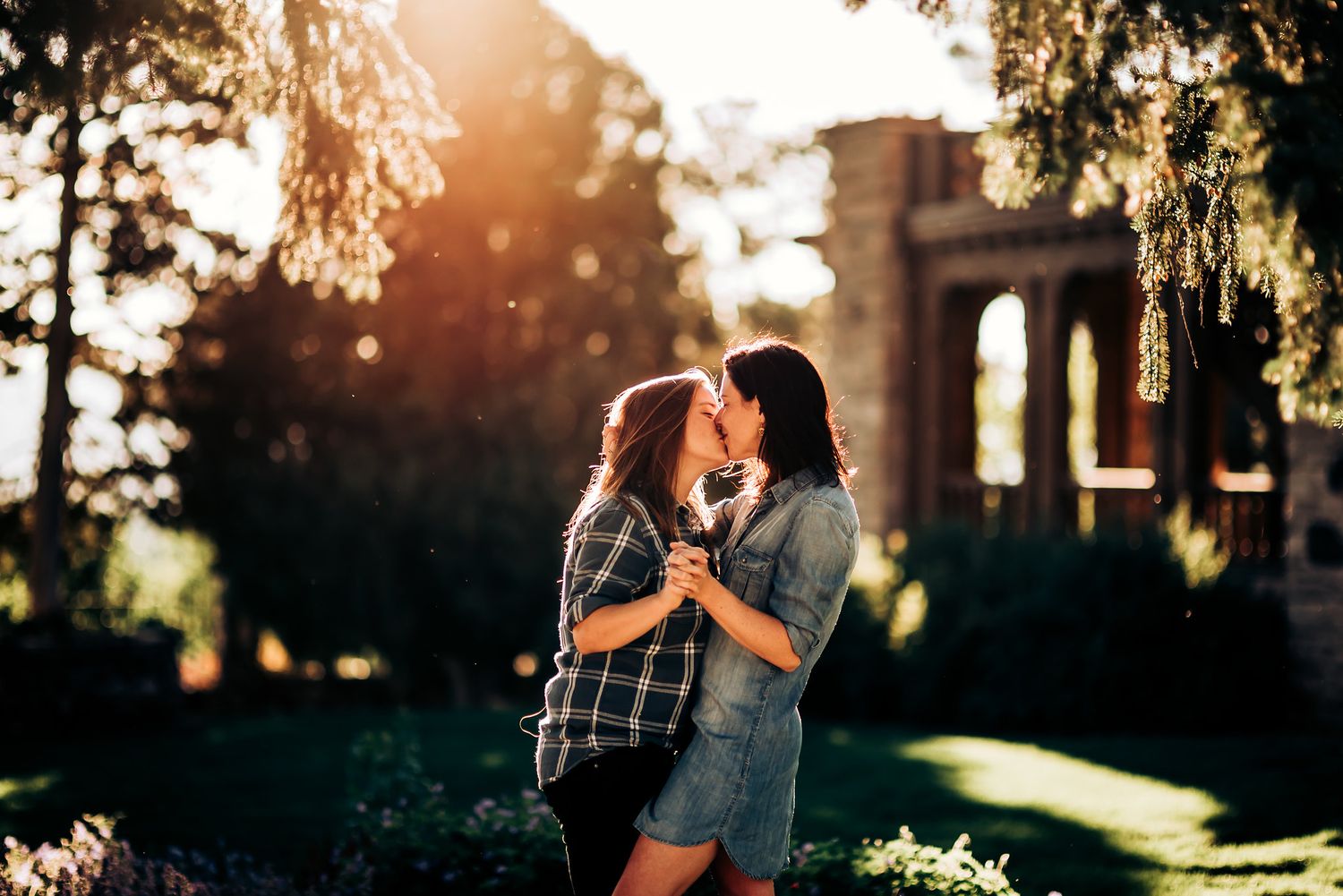 A romantic moment captured at sunset with stone architecture and trees in background.