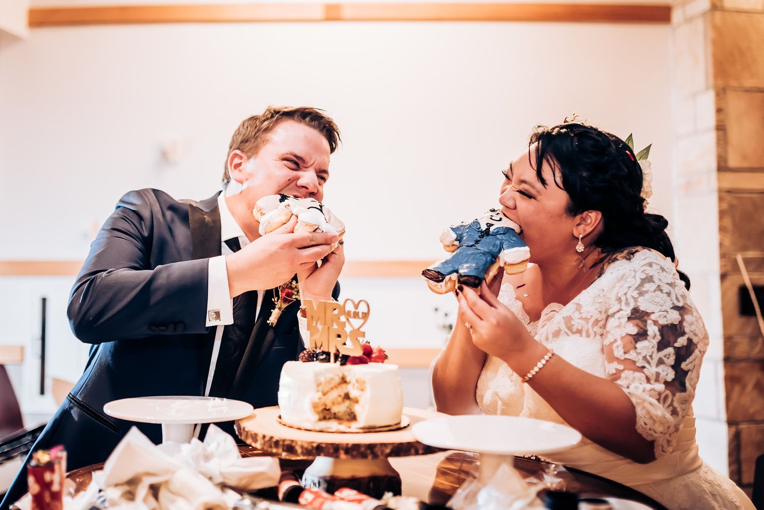 Couple playfully eating wedding cake together at their reception.