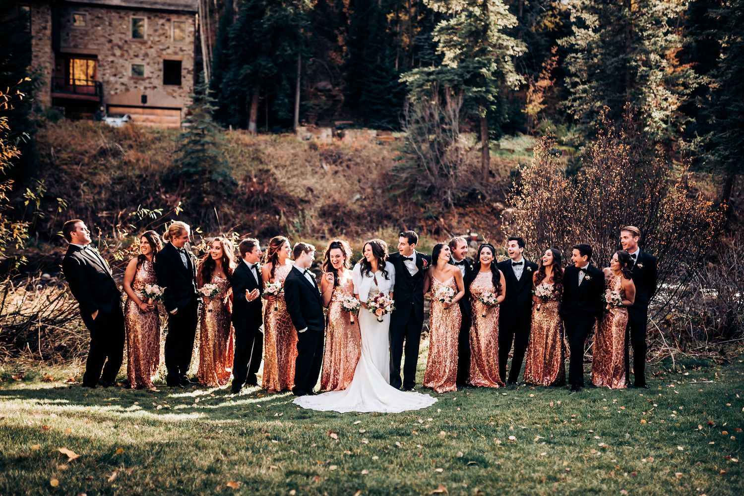 Wedding party lines up outdoors with bridesmaids in copper dresses against mountain scenery.
