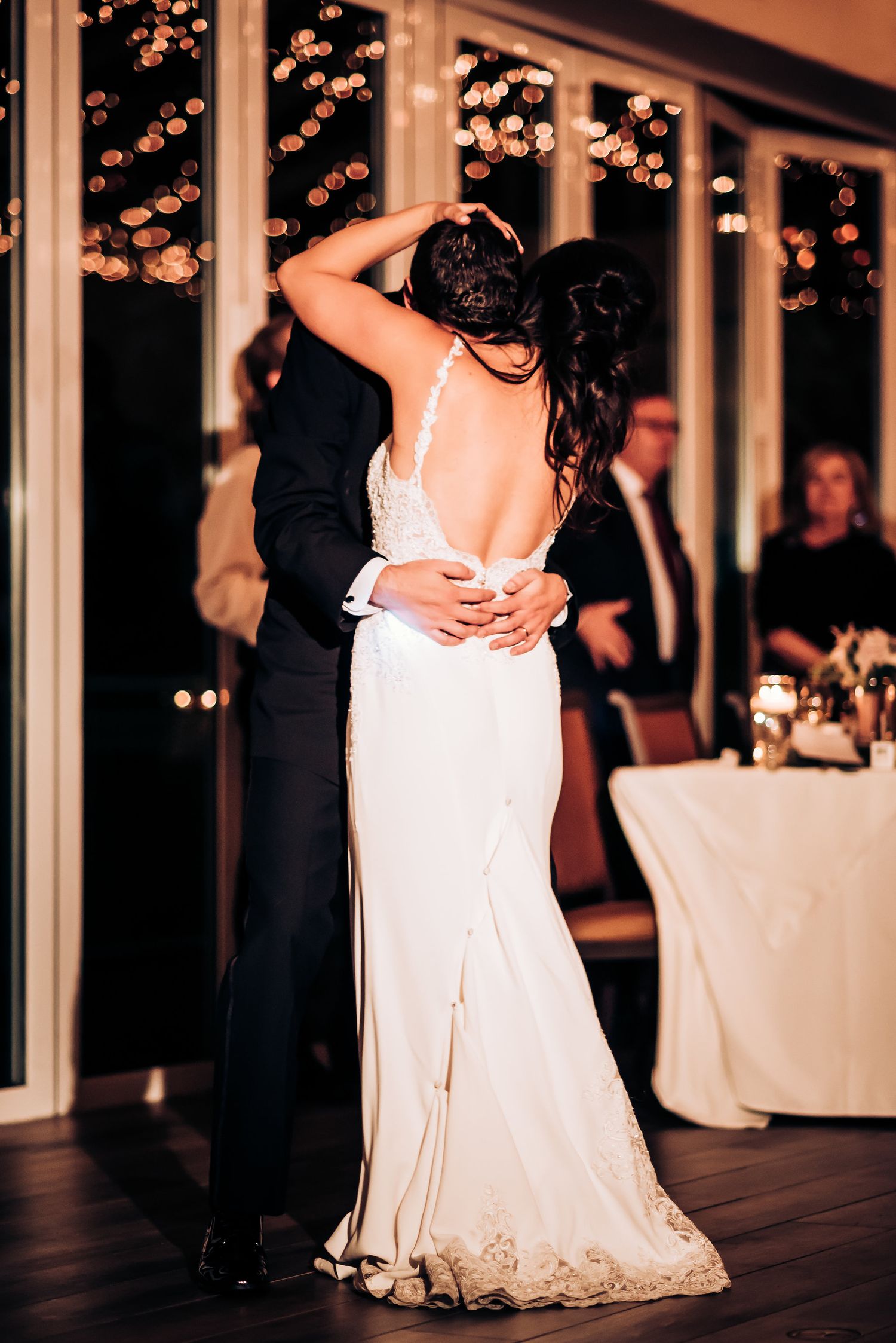 Elegant couple embraces during romantic slow dance at wedding reception.