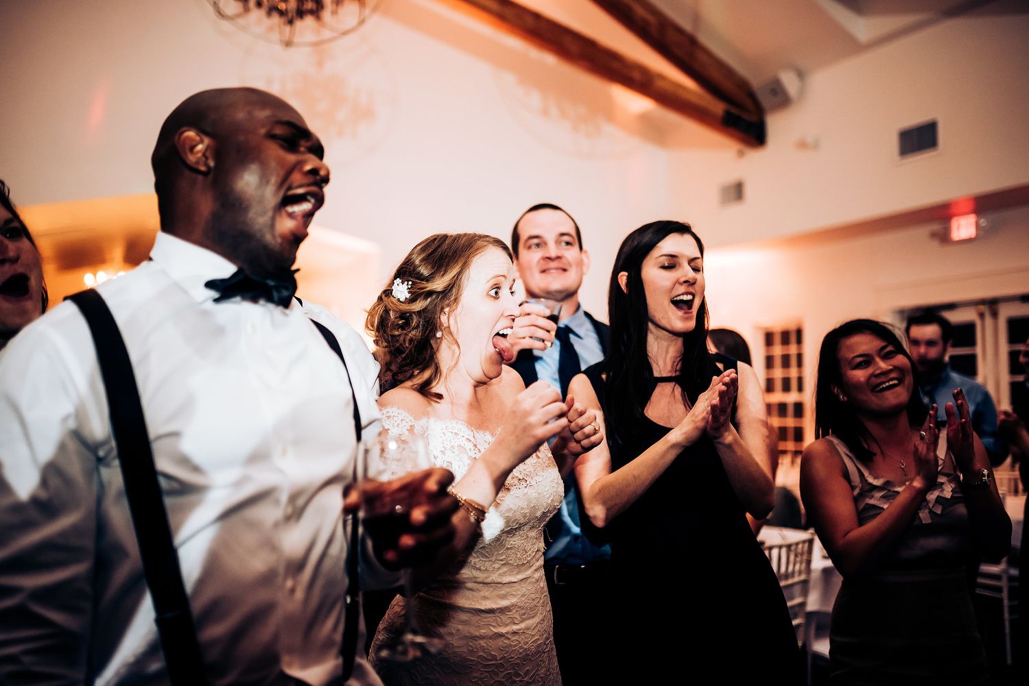 Wedding reception party with guests singing and celebrating in a warmly lit venue.