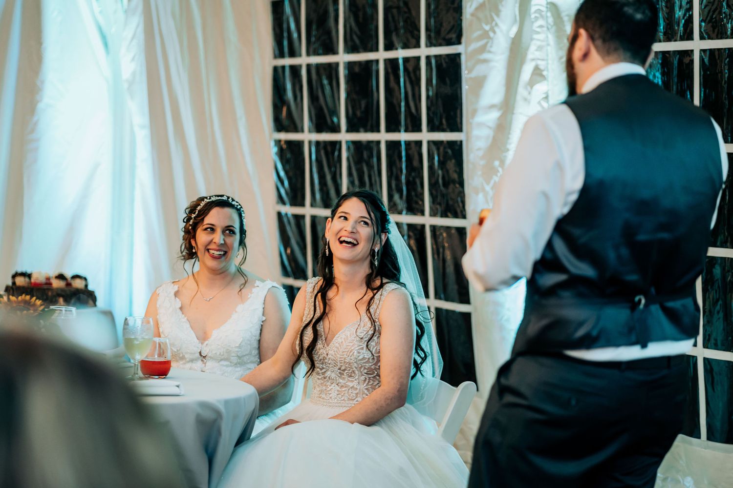 Wedding reception scene indoors with couples seated in white dresses.