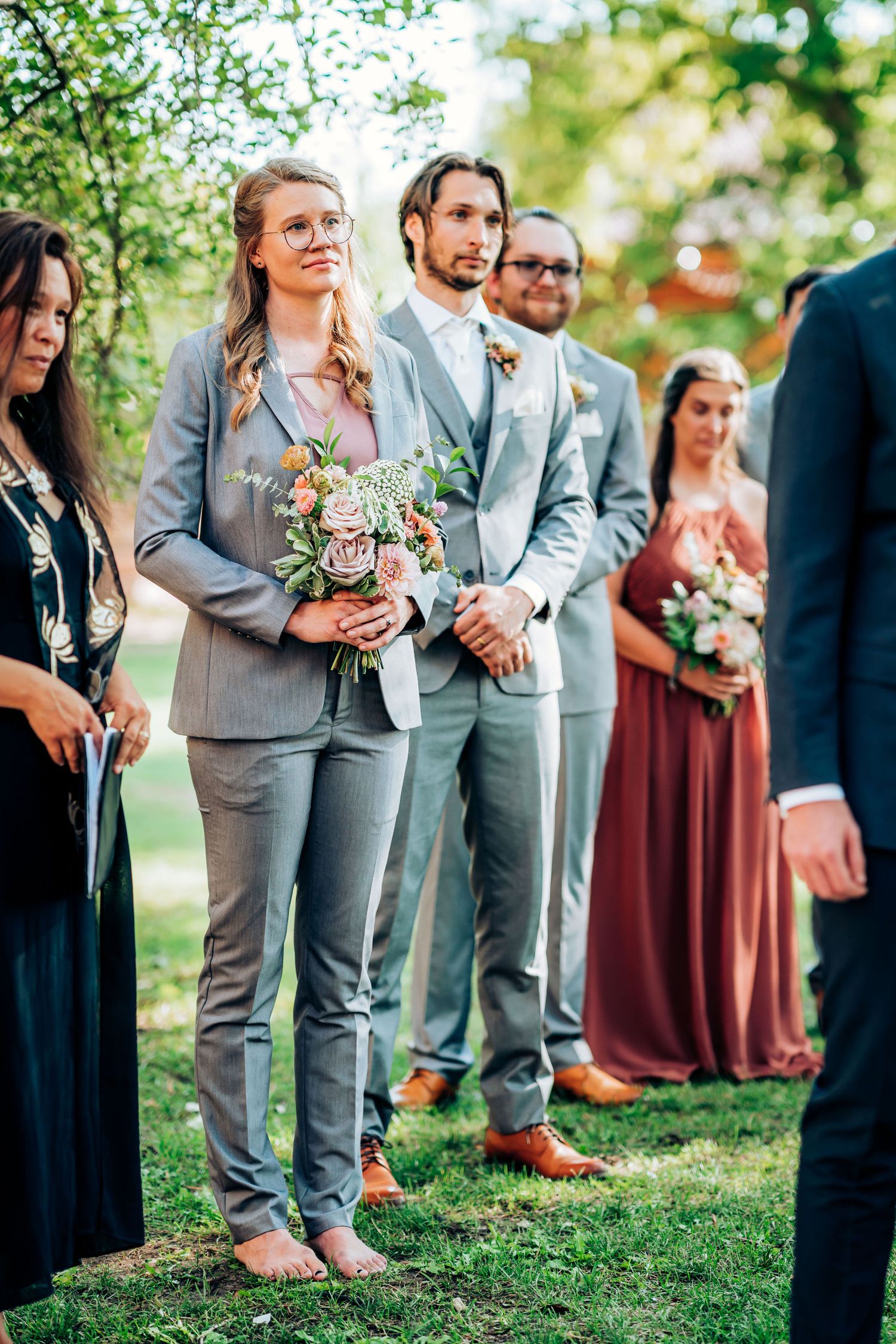Wedding party lined up outdoors wearing gray suits and burgundy dresses.