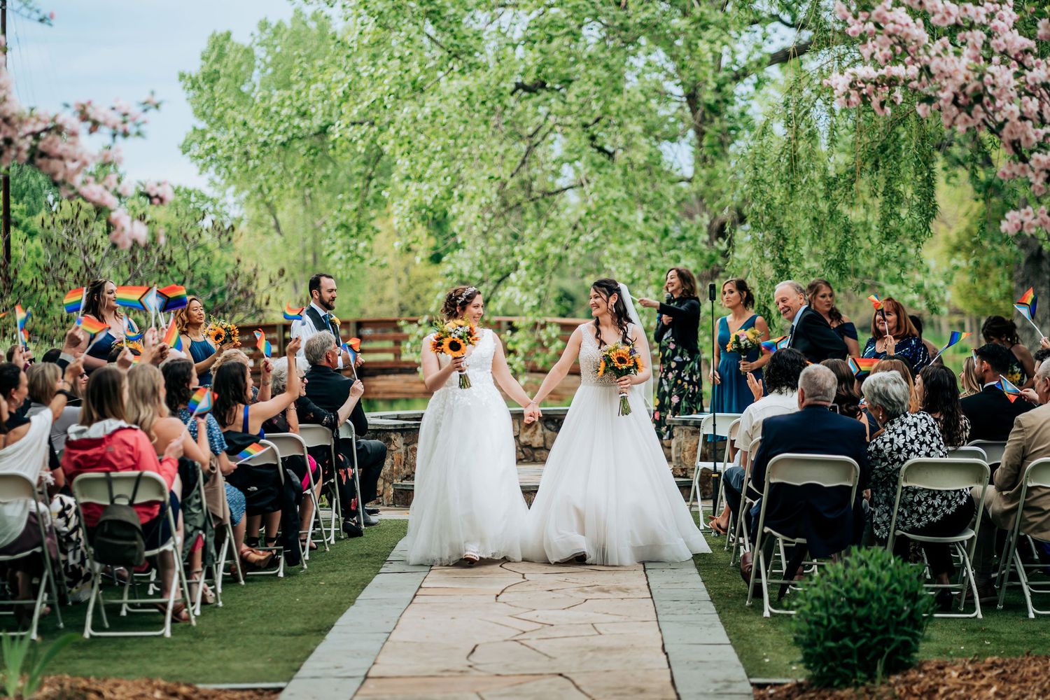 Wedding ceremony held outdoors with guests seated on folding chairs under blooming trees.