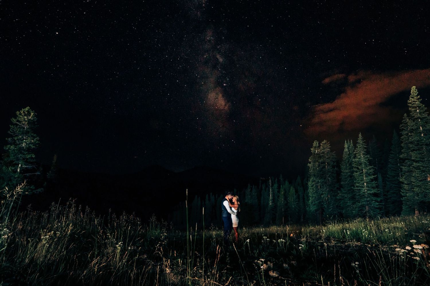 Dramatic nighttime wedding photo with mountain silhouettes in background.