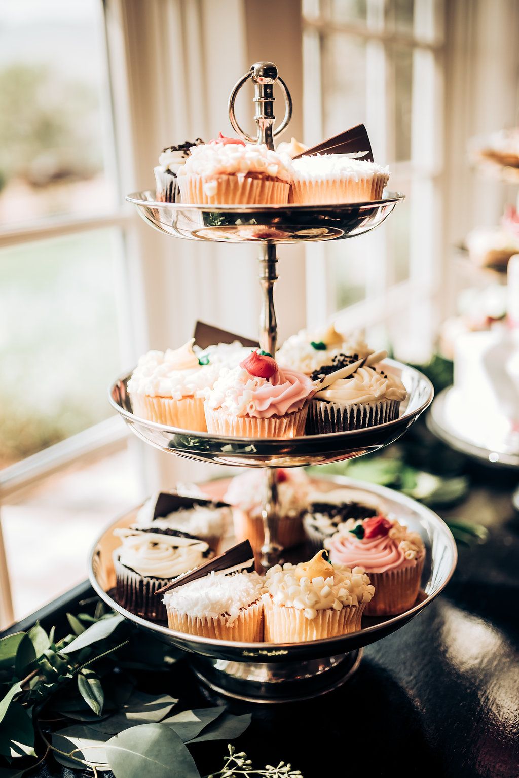 Three-tiered silver stand with decorated cupcakes and bride and groom cake topper.