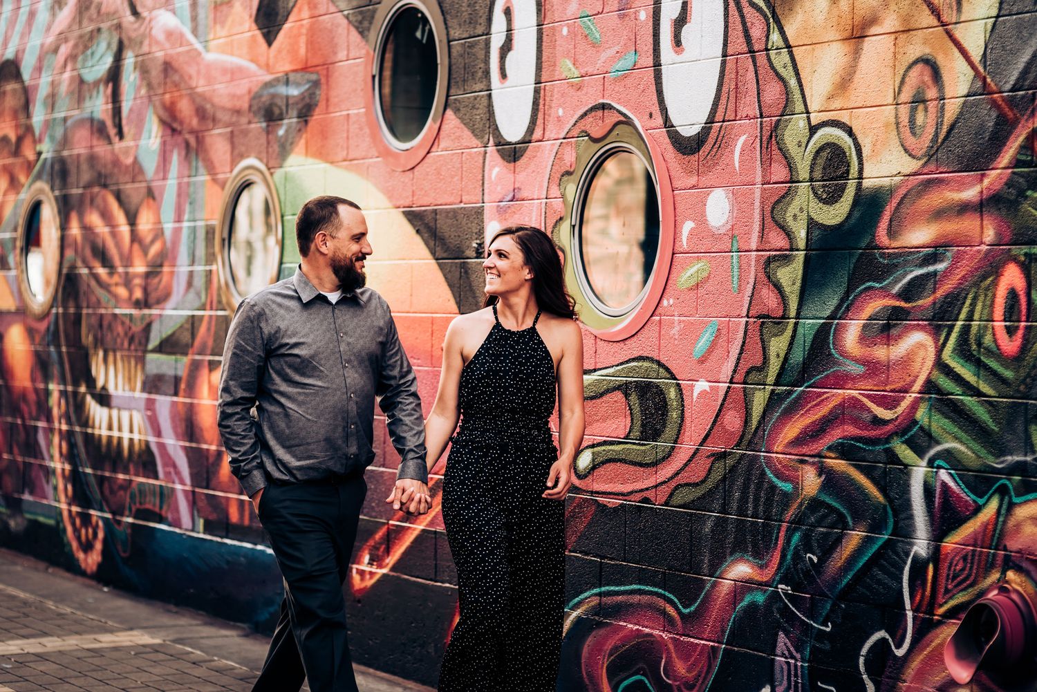 A couple stands in front of a pink and orange graffiti wall with circular patterns.