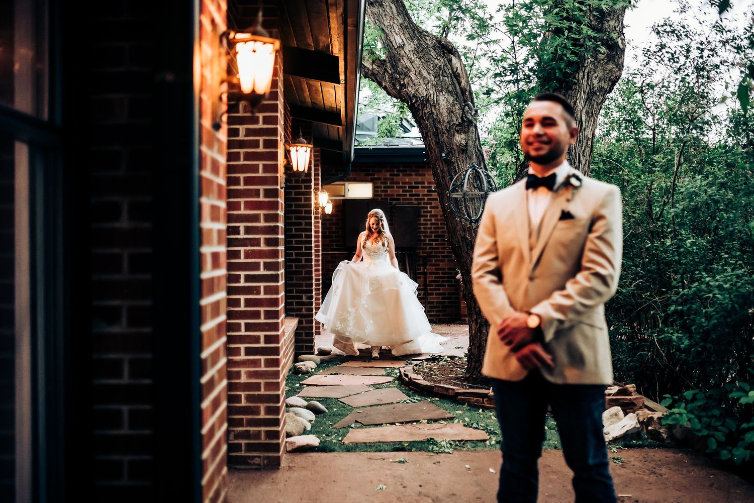 Artistic wedding photo with brick wall and lantern lighting creating romantic ambiance.