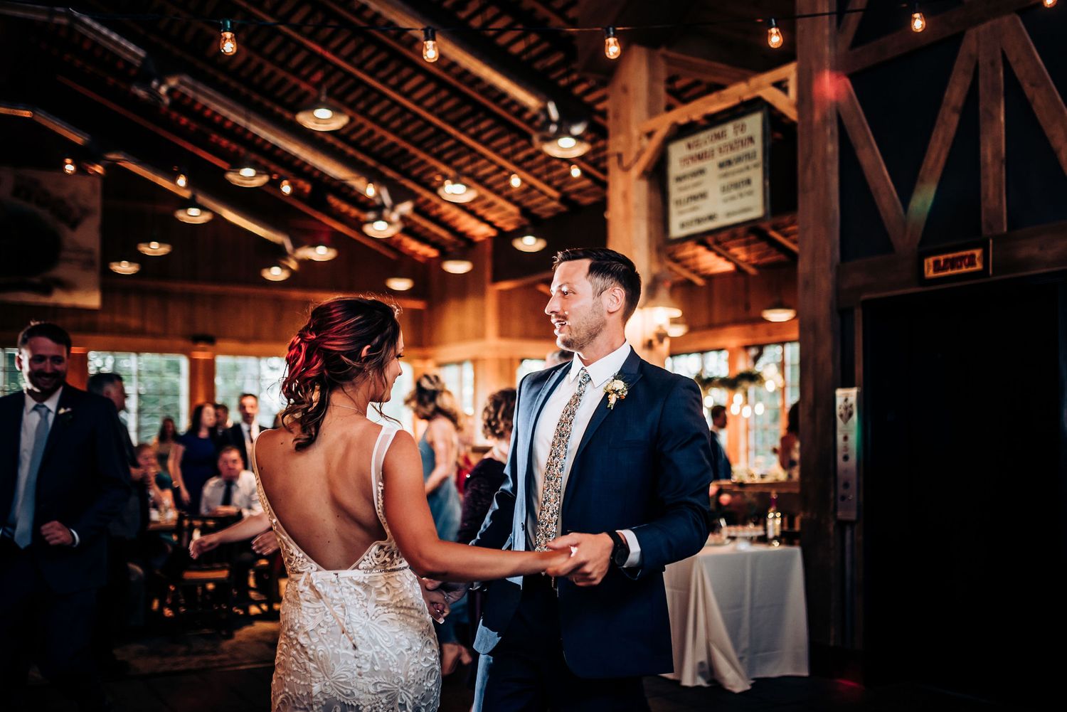 A couple dances beneath rustic wooden beams at their wedding reception.