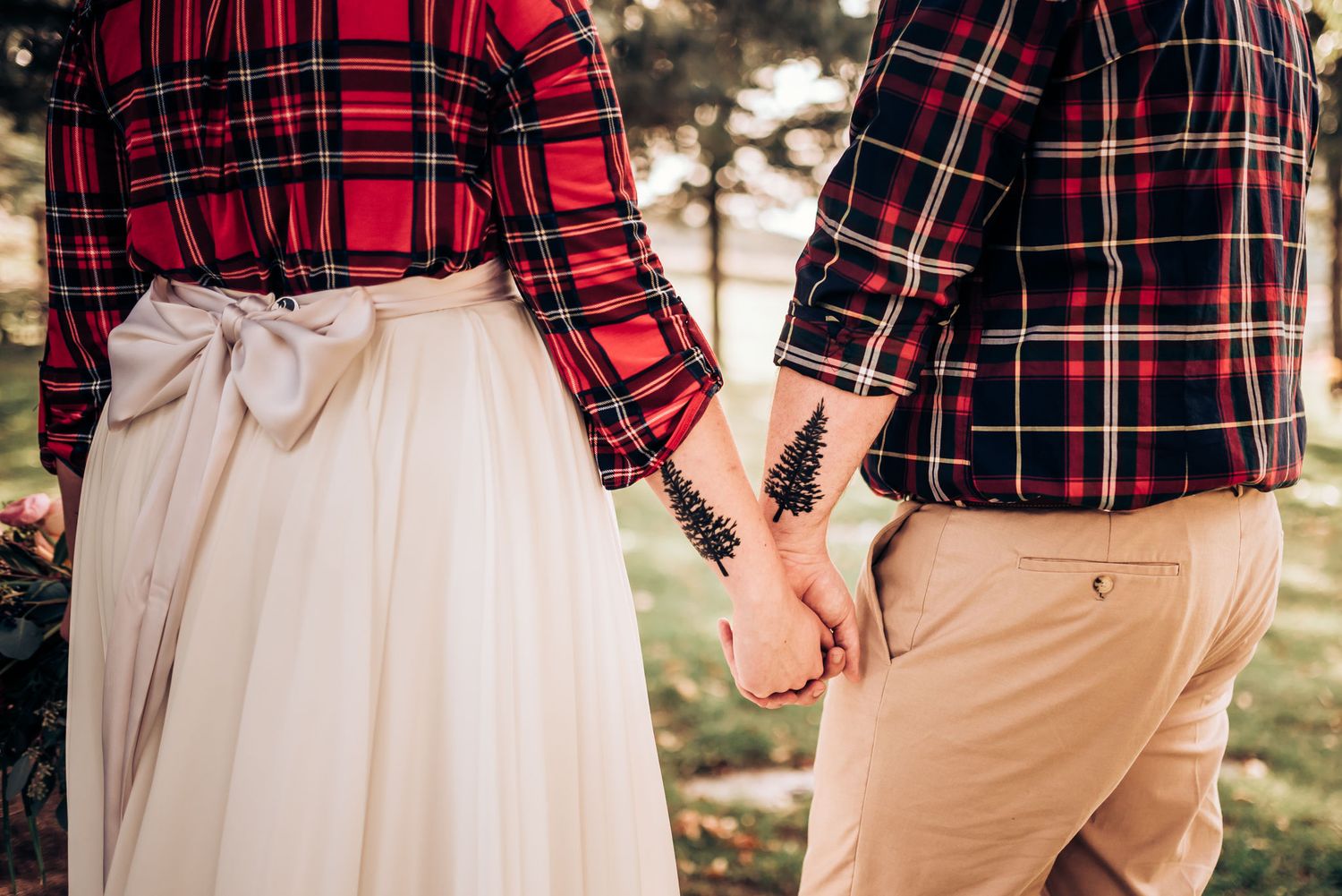 A couple wearing matching red plaid shirts hold hands while dressed in coordinated wedding attire.