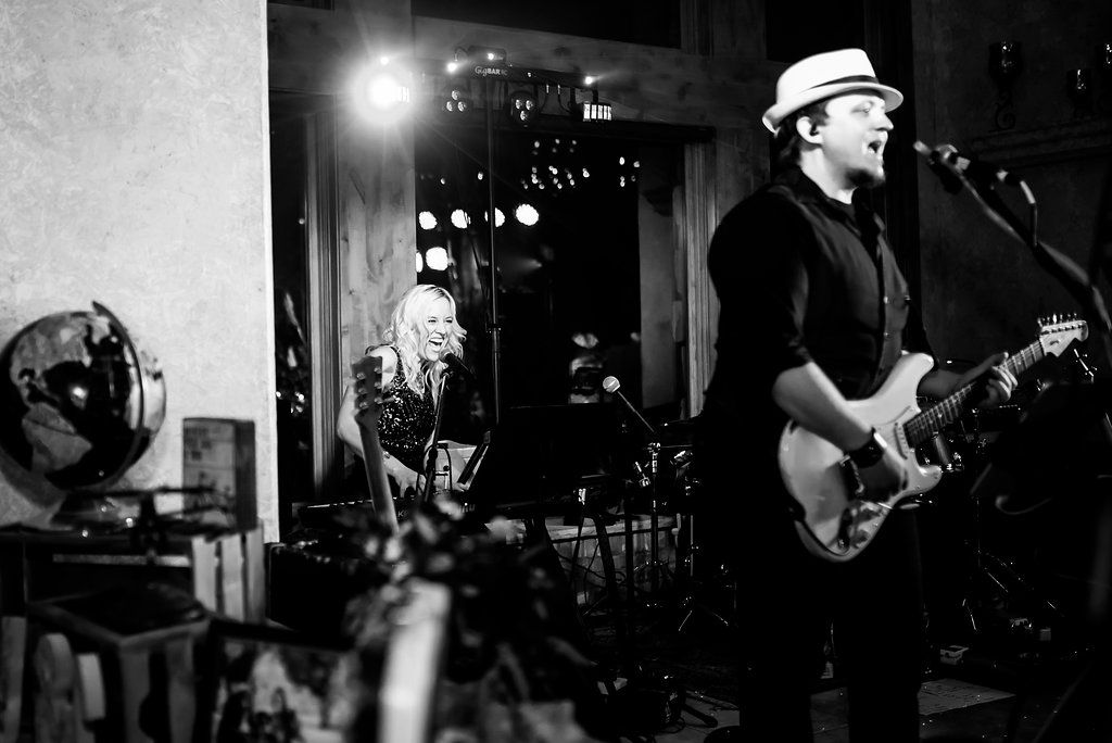 Black and white photo of live band performing at indoor venue with stage lighting.
