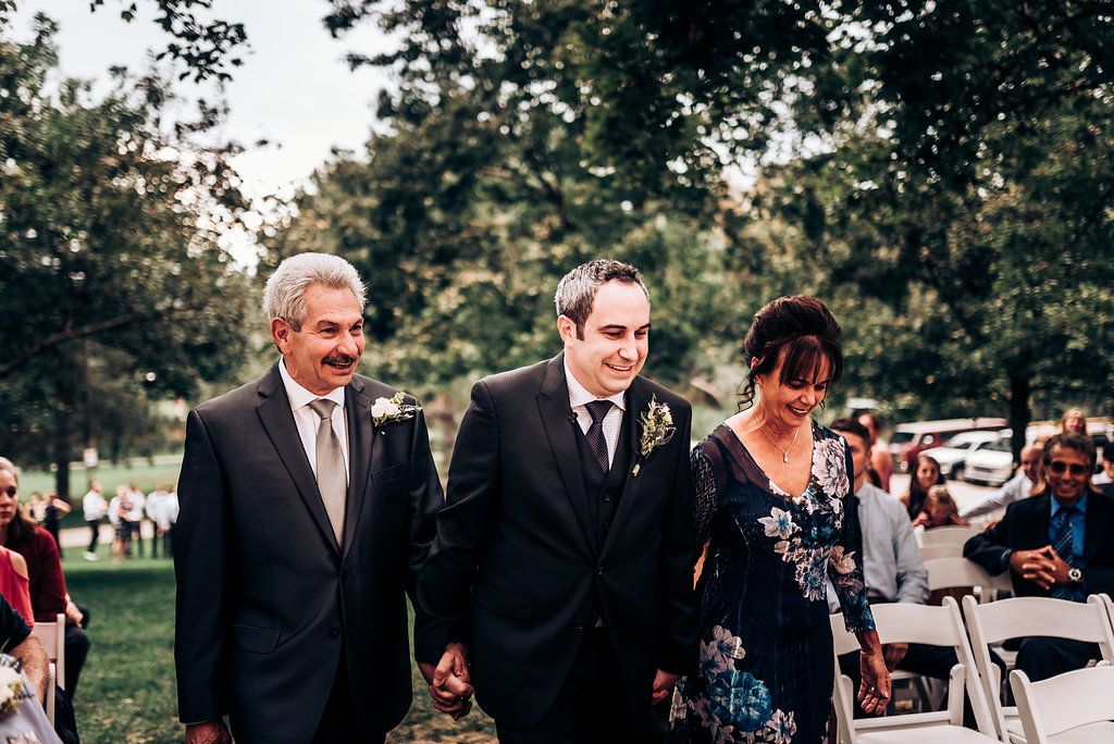 Wedding ceremony processional on an outdoor lawn with guests seated.