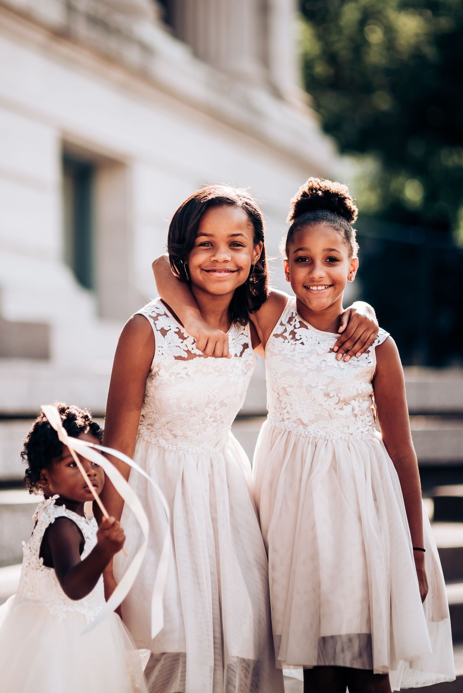 Young attendants in matching white dresses share a joyful moment outside.