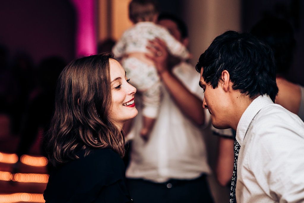 Two people sharing a fun dancing moment at an indoor celebration with pink lighting.