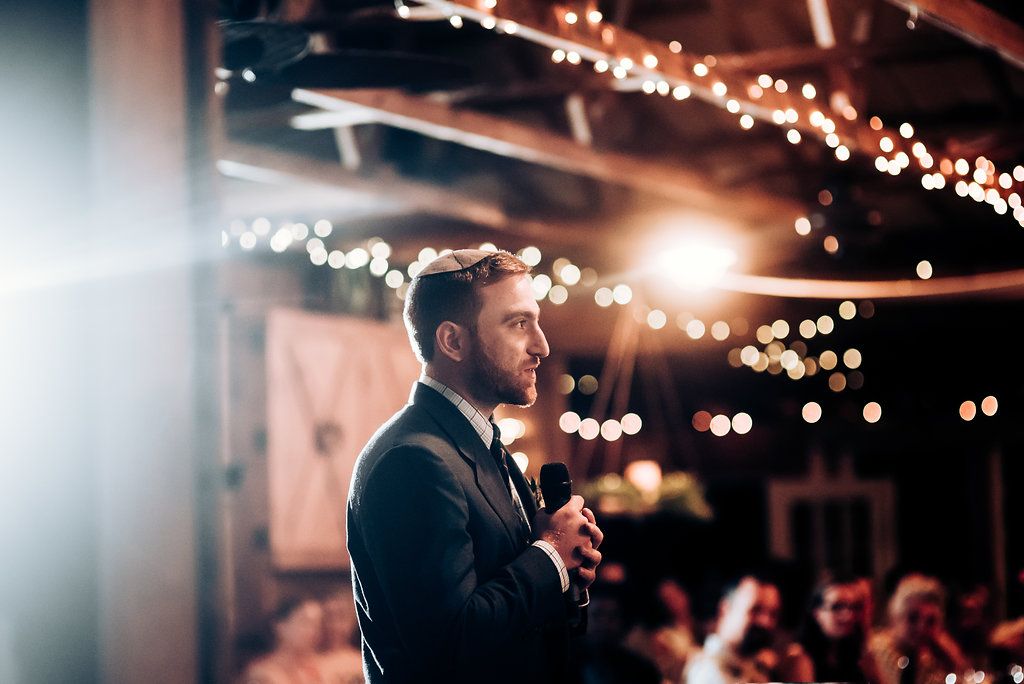 Person giving heartfelt speech at rustic indoor reception with ambient lighting.