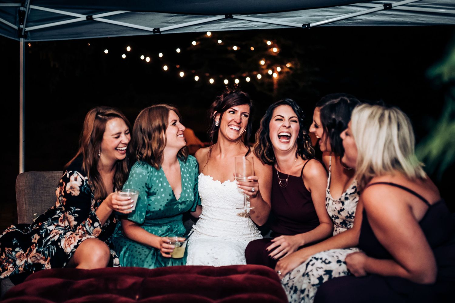 Candid group moment showing wedding party laughing together on red seating.