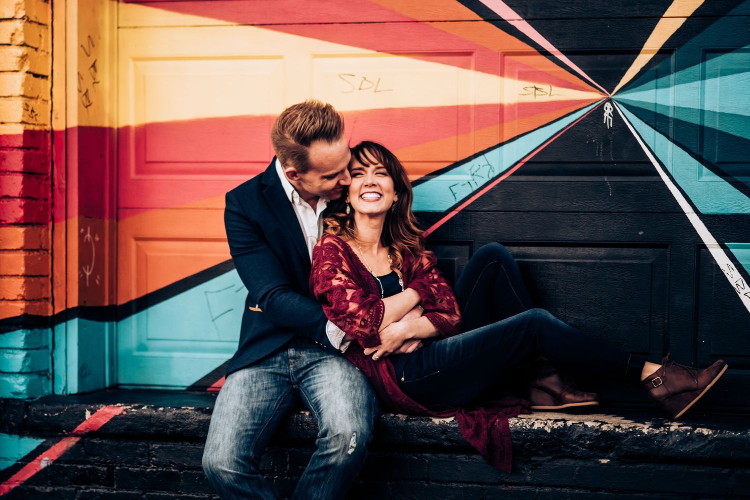 A couple relaxes against a wall featuring a striking geometric pattern in red and blue.