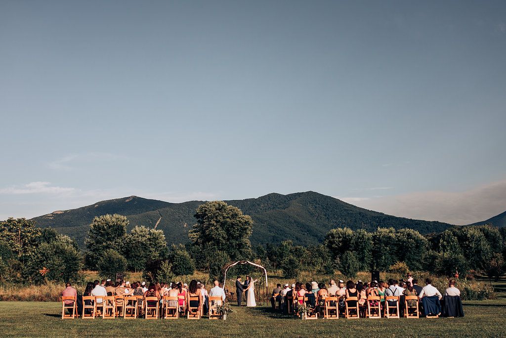 An outdoor wedding ceremony set against scenic mountain views with wooden chairs arranged on a grass lawn.