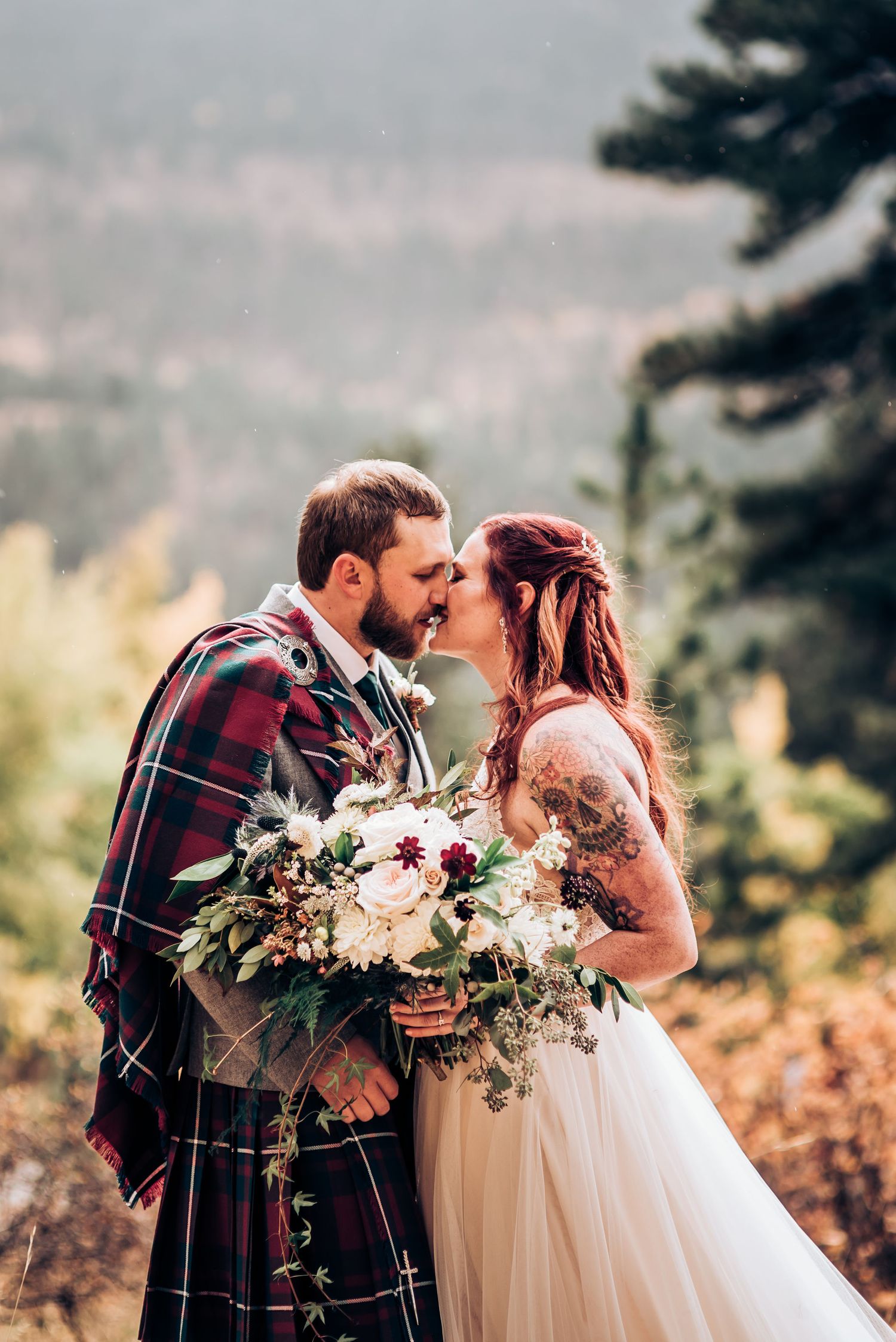 Intimate wedding moment with Scottish tartan and flowing bouquet against mountain backdrop.