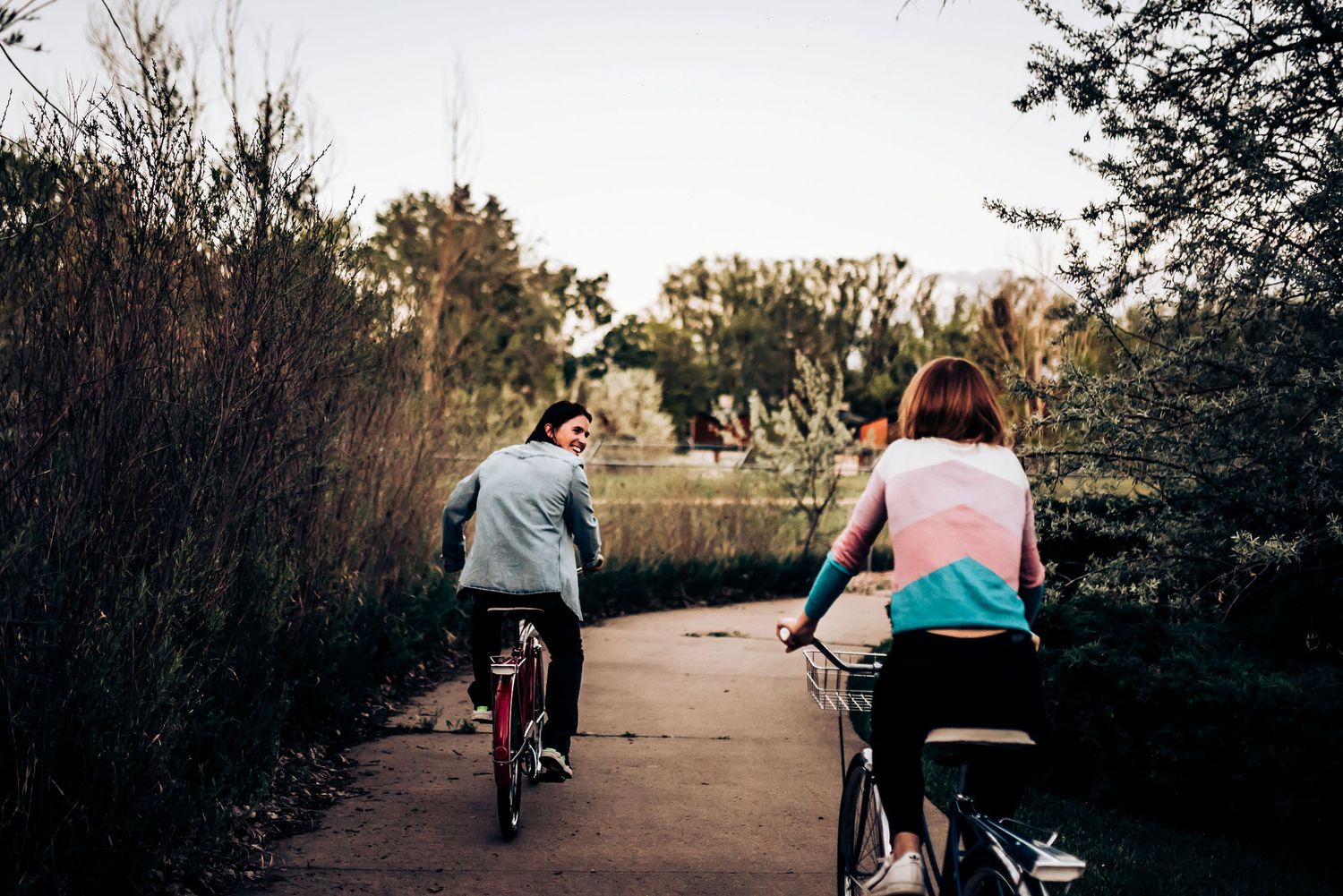 Two people ride bicycles down a paved path during sunset.