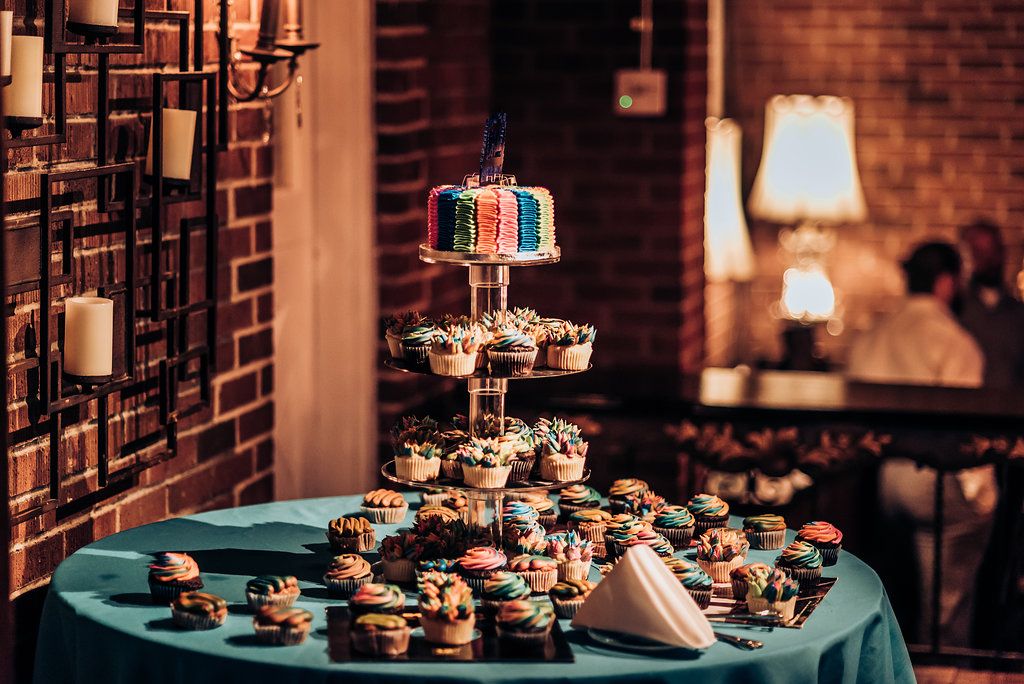 Multi-tiered display of wedding cupcakes and cake with candlelit brick wall background.