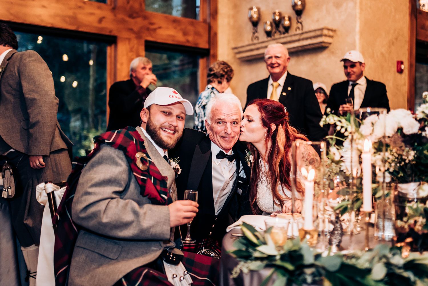 Wedding guests share laughter and drinks during an intimate reception dinner at a rustic venue.