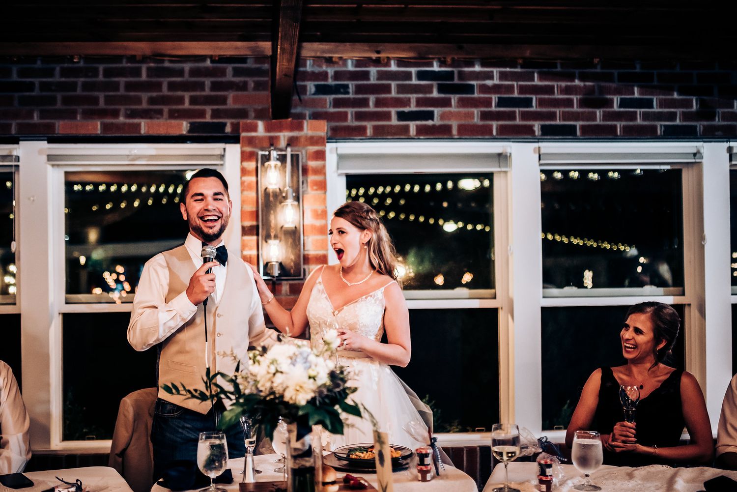 A couple shares joyful moments during wedding reception toasts at an indoor venue.