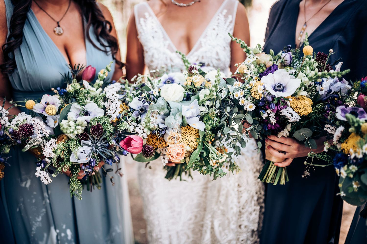 Beautiful wedding bouquets featuring blue, white and pink flowers held against blue bridesmaid dresses.