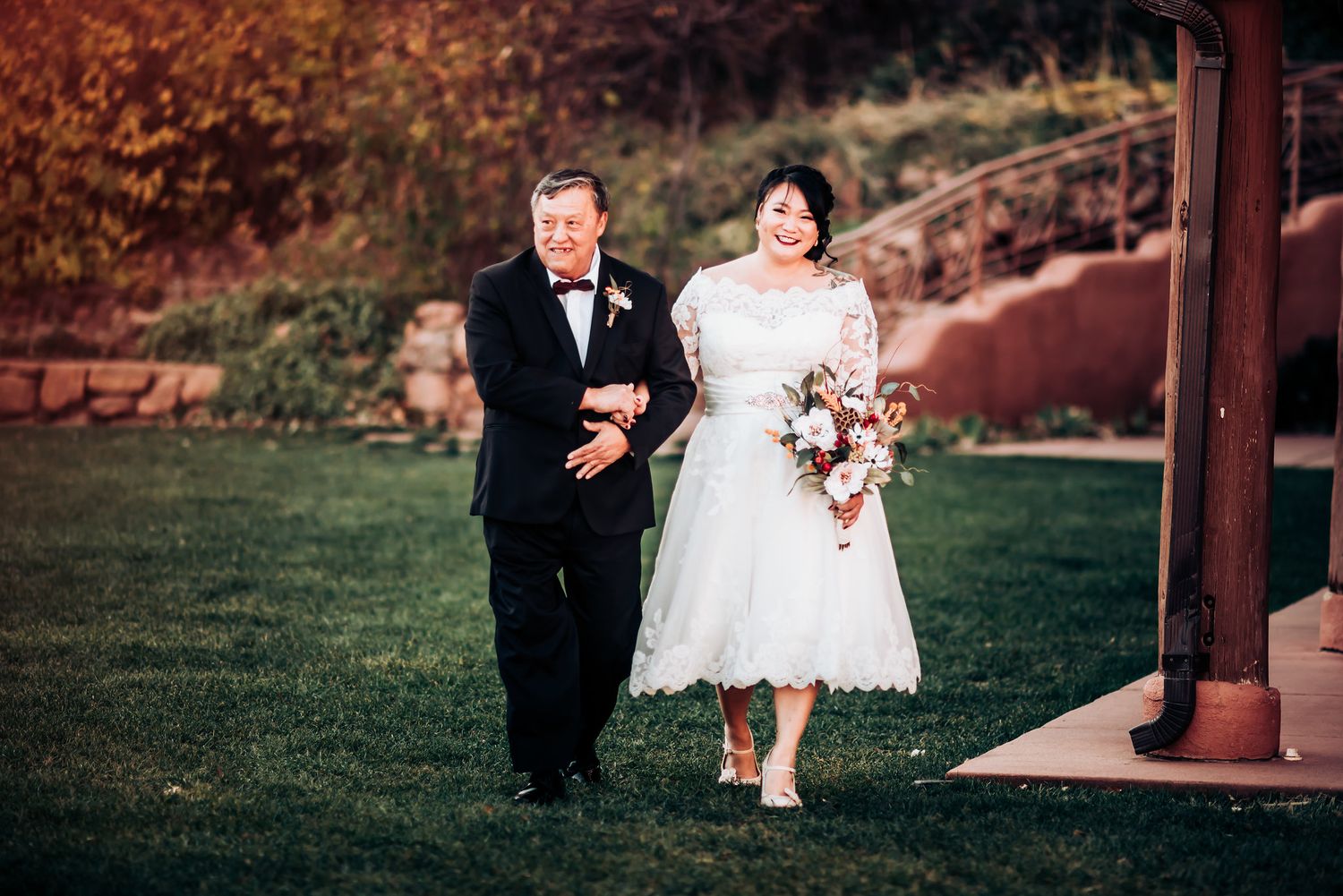A couple walks down a garden path at a rustic outdoor wedding venue.