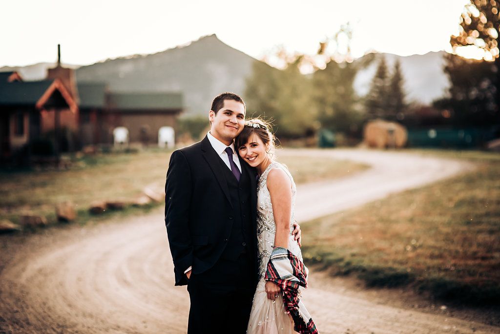 A couple poses together on a country road at sunset with mountains in the background.