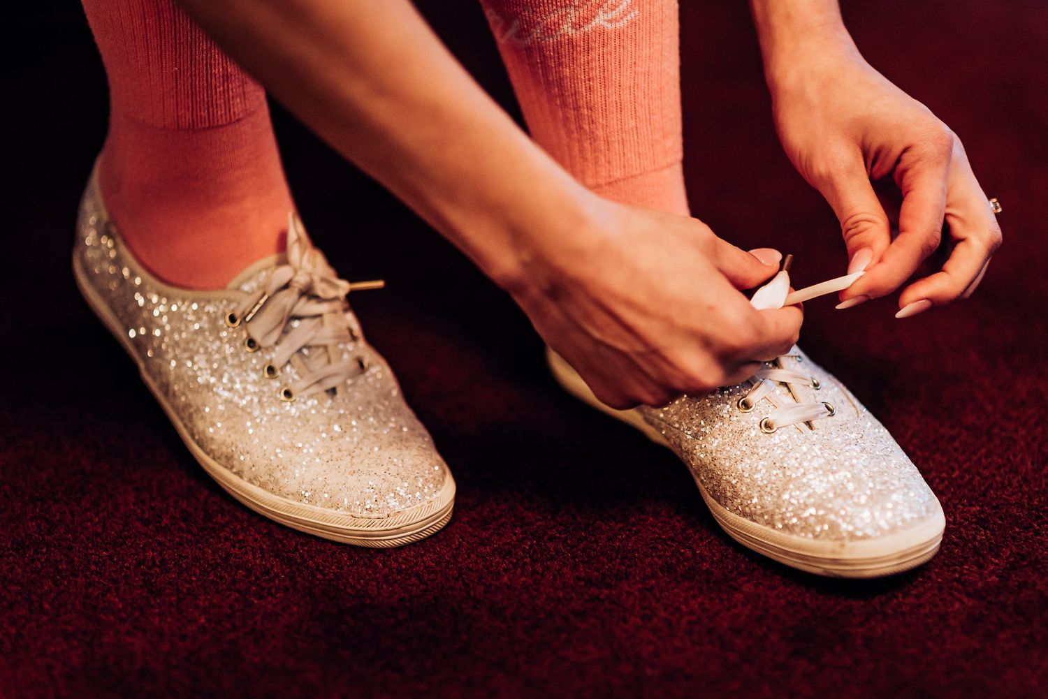 Hands tying sparkly beige sneakers with coral-colored socks.