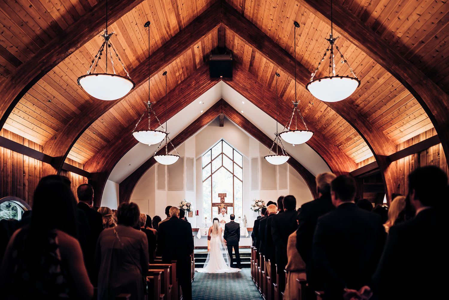 A beautiful church wedding ceremony under vaulted wooden ceilings with warm lighting.