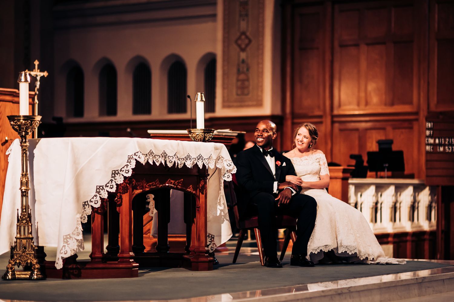 Couple sits together at the decorated church altar during their wedding ceremony.