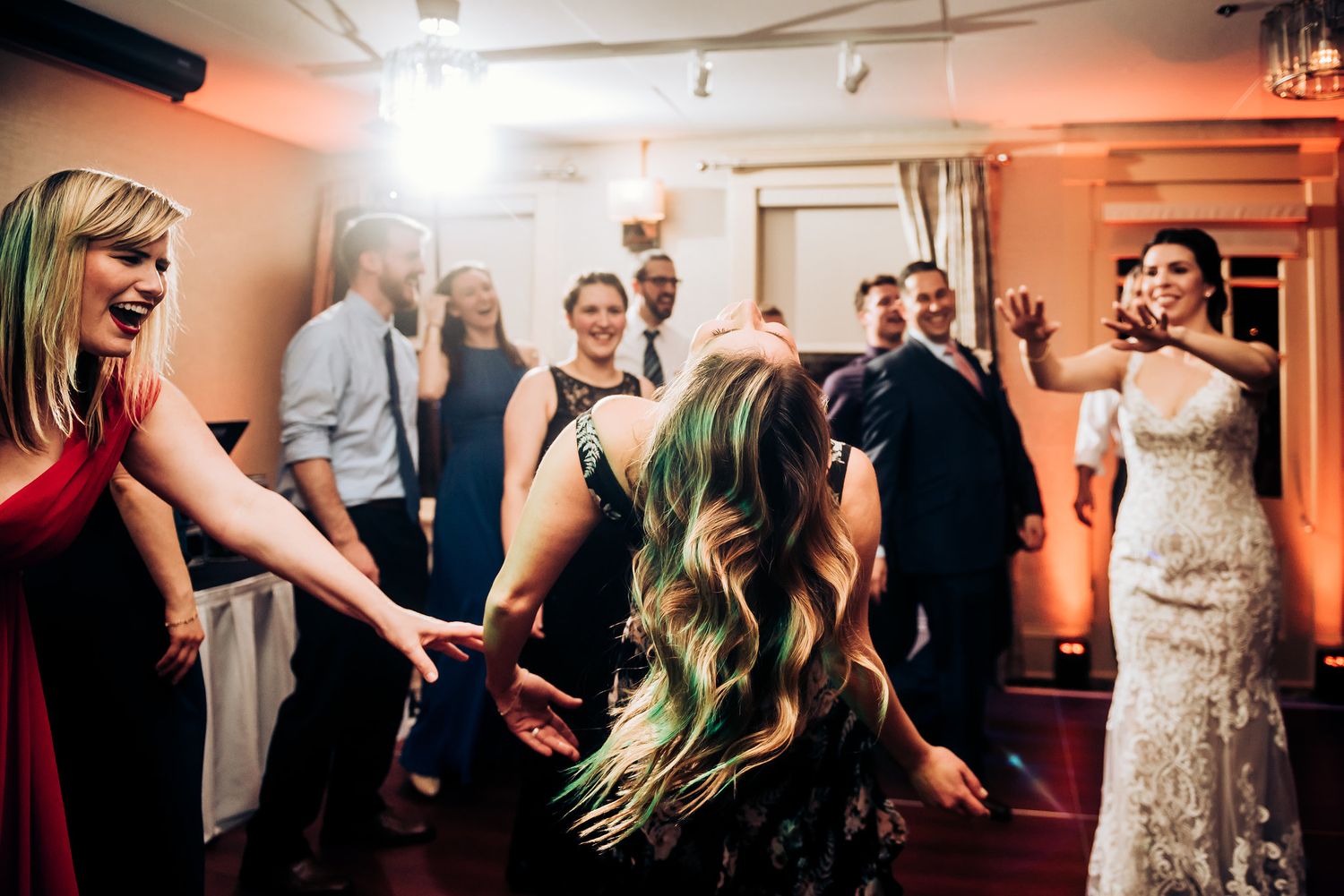 Wedding guests dancing and celebrating at indoor reception with atmospheric lighting.