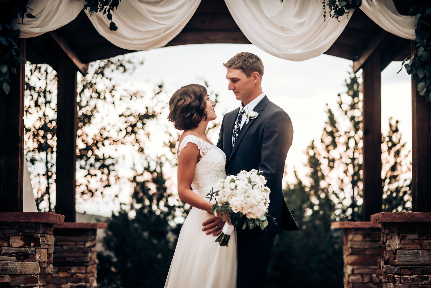 Romantic wedding portrait under white draped pavilion during golden hour.